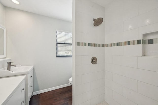 full bathroom with baseboards, toilet, tiled shower, wood finished floors, and vanity