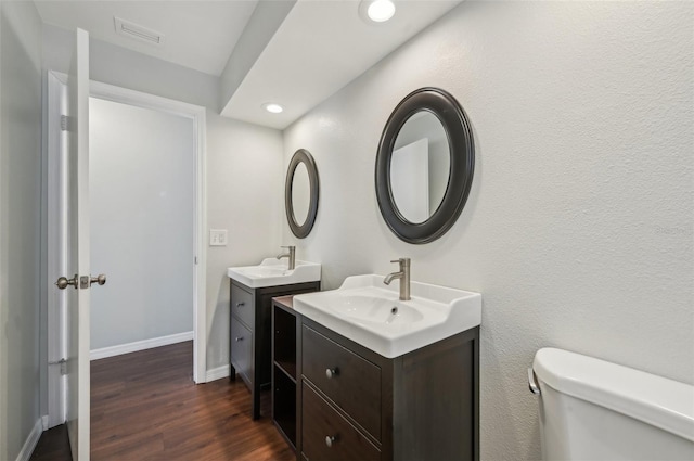 bathroom with two vanities, wood finished floors, visible vents, and a sink