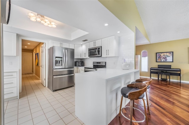 kitchen featuring tasteful backsplash, appliances with stainless steel finishes, a peninsula, white cabinets, and a raised ceiling