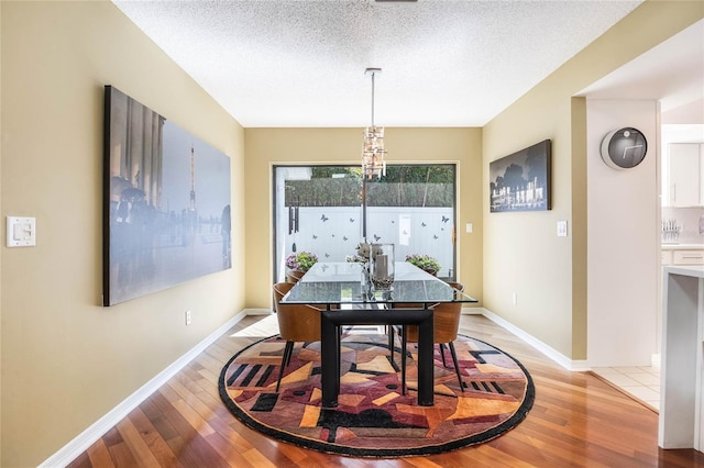 dining room featuring light wood-style flooring, baseboards, and a textured ceiling