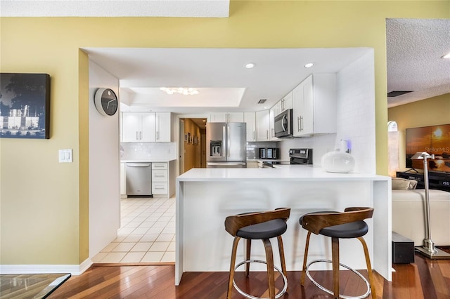 kitchen with backsplash, white cabinetry, appliances with stainless steel finishes, a breakfast bar area, and a peninsula