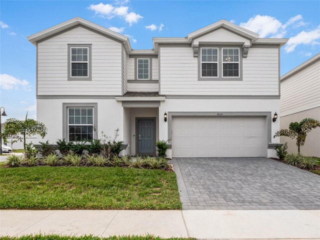 view of front facade with decorative driveway, a front yard, an attached garage, and stucco siding