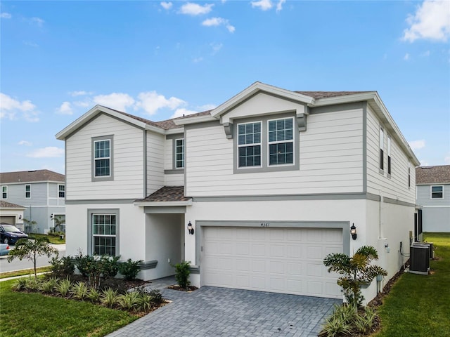 traditional-style house with a front lawn, central AC unit, stucco siding, decorative driveway, and a garage