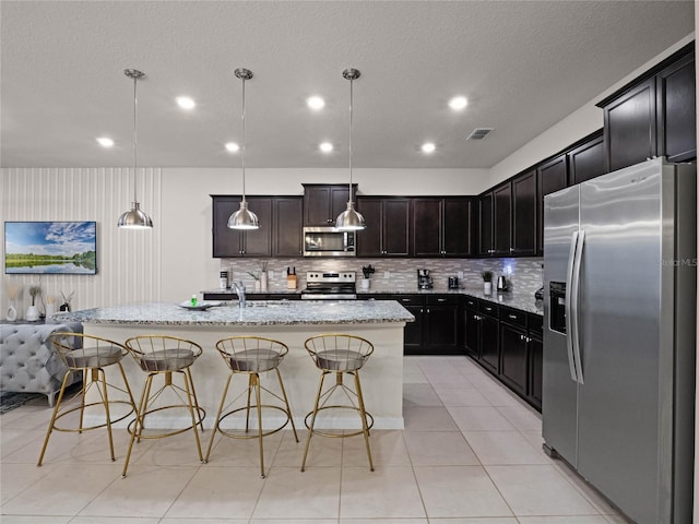 kitchen with stainless steel appliances, light stone countertops, visible vents, and a breakfast bar area