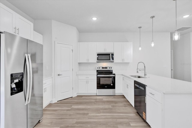 kitchen with light wood finished floors, a peninsula, stainless steel appliances, white cabinetry, and a sink