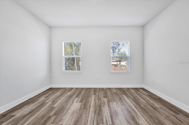 empty room featuring a healthy amount of sunlight, baseboards, and wood finished floors