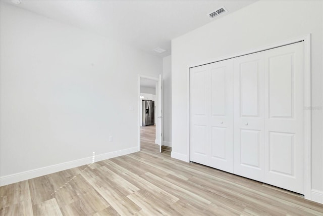 unfurnished bedroom featuring light wood finished floors, visible vents, baseboards, stainless steel fridge with ice dispenser, and a closet