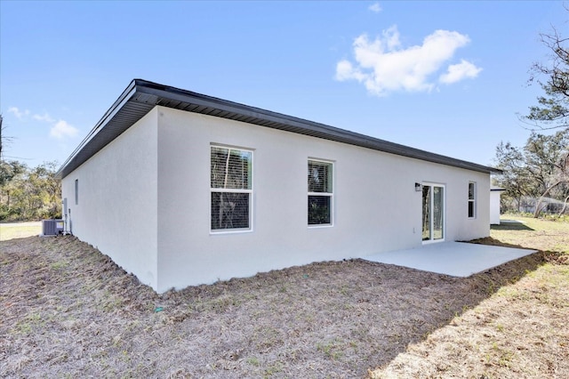 rear view of house with stucco siding, central AC unit, and a patio area