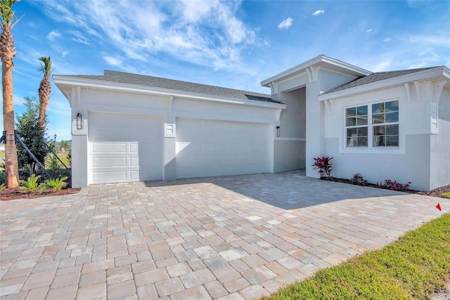 view of front facade featuring decorative driveway, an attached garage, a shingled roof, and stucco siding