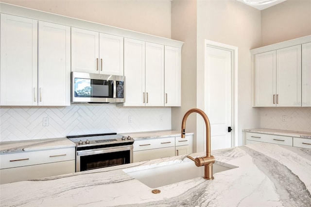 kitchen featuring white cabinetry, light stone countertops, appliances with stainless steel finishes, and a sink