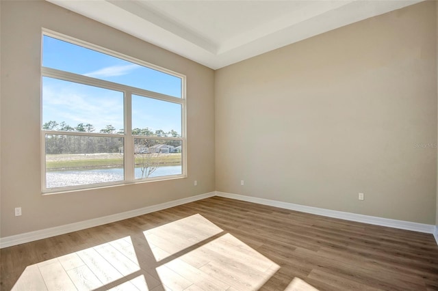 empty room with wood finished floors, baseboards, and a water view