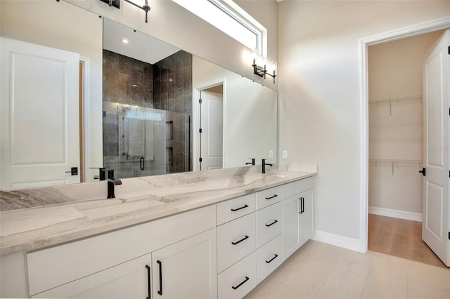 full bath with a walk in closet, a sink, a shower stall, double vanity, and baseboards