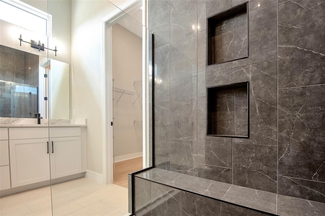 bathroom featuring a spacious closet, baseboards, vanity, and walk in shower