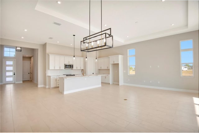 kitchen with white cabinetry, stainless steel microwave, baseboards, and a tray ceiling