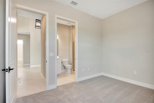 unfurnished bedroom with visible vents, ensuite bath, light tile patterned flooring, baseboards, and light colored carpet