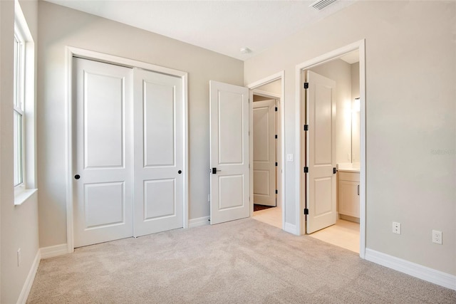 unfurnished bedroom with visible vents, baseboards, light carpet, ensuite bathroom, and a closet