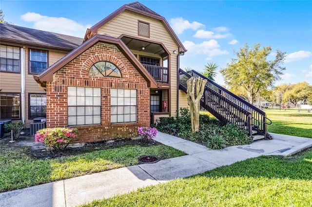 exterior space with stairs, a front yard, brick siding, and central AC