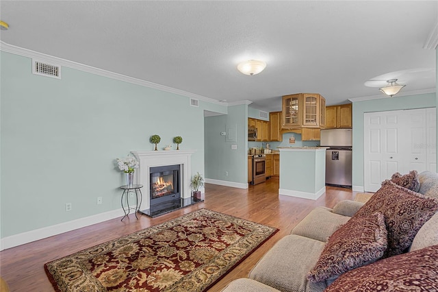 living area with baseboards, light wood-style floors, a glass covered fireplace, and crown molding