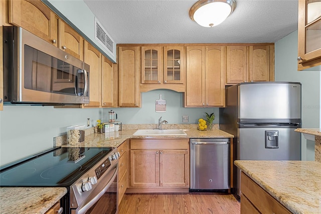 kitchen featuring visible vents, glass insert cabinets, appliances with stainless steel finishes, light wood-style floors, and a sink