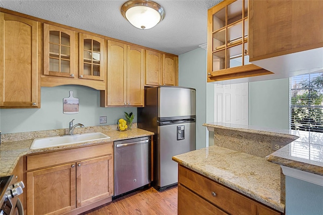 kitchen featuring glass insert cabinets, stainless steel appliances, light wood-style floors, a textured ceiling, and a sink