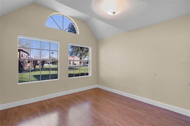 empty room featuring vaulted ceiling, wood finished floors, and baseboards