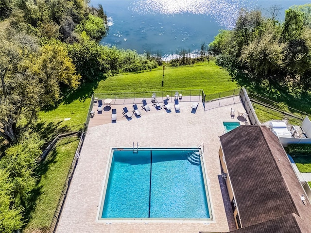 view of swimming pool featuring fence, a lawn, and a water view