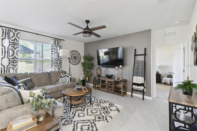 living area featuring tile patterned floors, baseboards, visible vents, and ceiling fan