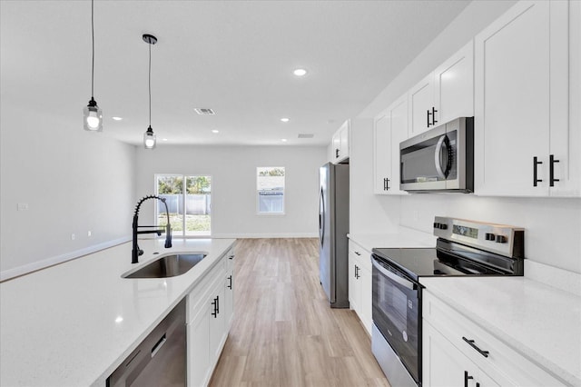 kitchen with visible vents, a sink, white cabinetry, stainless steel appliances, and hanging light fixtures