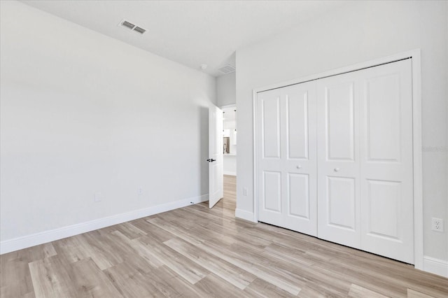 unfurnished bedroom with a closet, visible vents, light wood-style floors, and baseboards