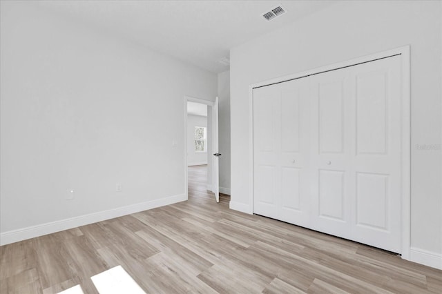 unfurnished bedroom featuring light wood finished floors, visible vents, a closet, and baseboards