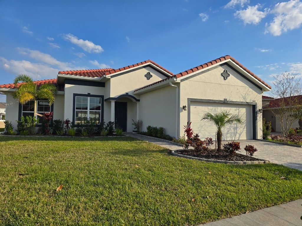 mediterranean / spanish home with driveway, an attached garage, stucco siding, a front lawn, and a tiled roof