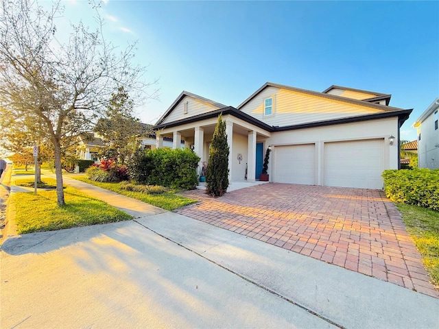 view of front of house with decorative driveway, an attached garage, and stucco siding