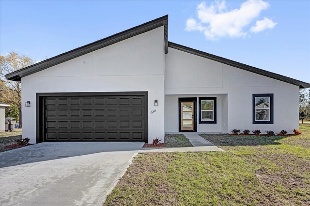 view of front of house with stucco siding, a front yard, a garage, and driveway