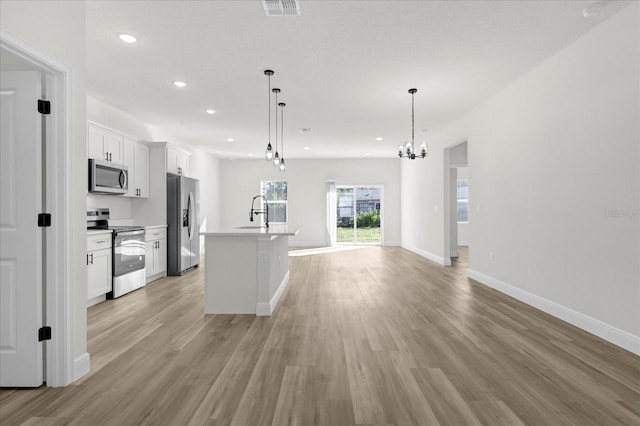 kitchen featuring a kitchen island with sink, open floor plan, white cabinetry, stainless steel appliances, and light wood finished floors