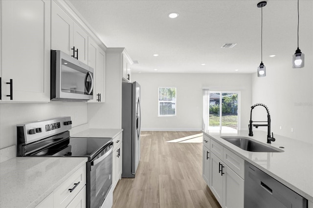 kitchen with visible vents, decorative light fixtures, white cabinets, stainless steel appliances, and a sink