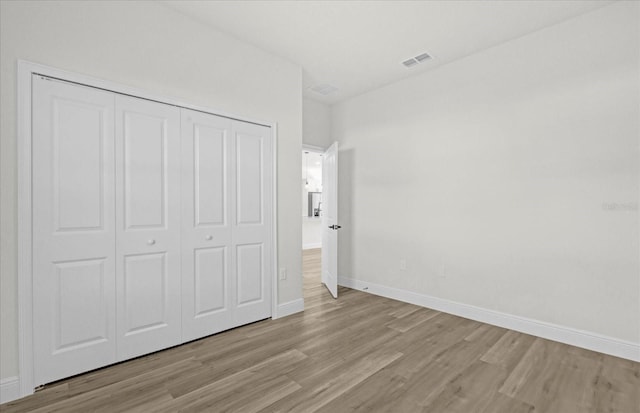 unfurnished bedroom featuring visible vents, baseboards, a closet, and wood finished floors