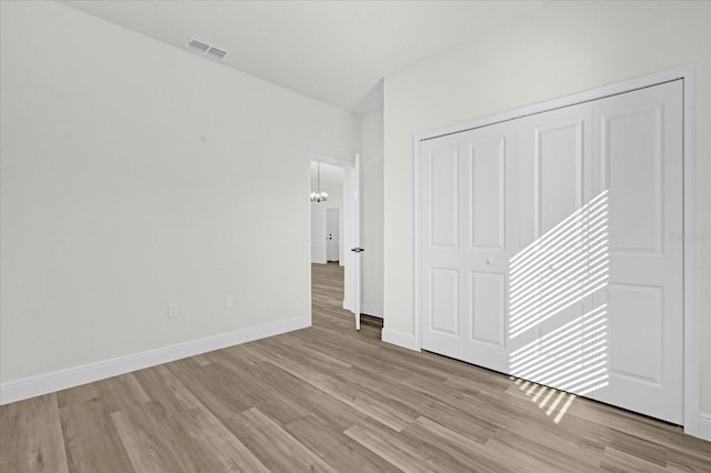 unfurnished bedroom with visible vents, baseboards, a closet, a notable chandelier, and light wood-type flooring