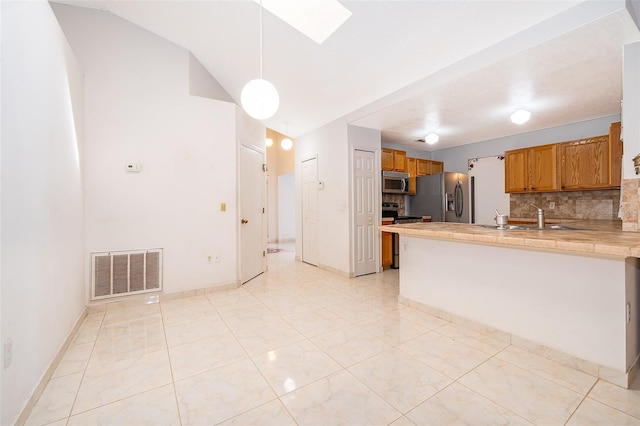 kitchen with visible vents, a peninsula, a sink, stainless steel appliances, and brown cabinets