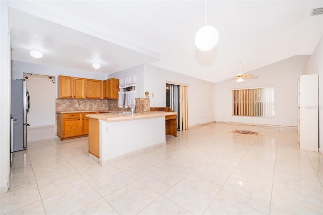 kitchen with open floor plan, freestanding refrigerator, a peninsula, brown cabinetry, and light countertops