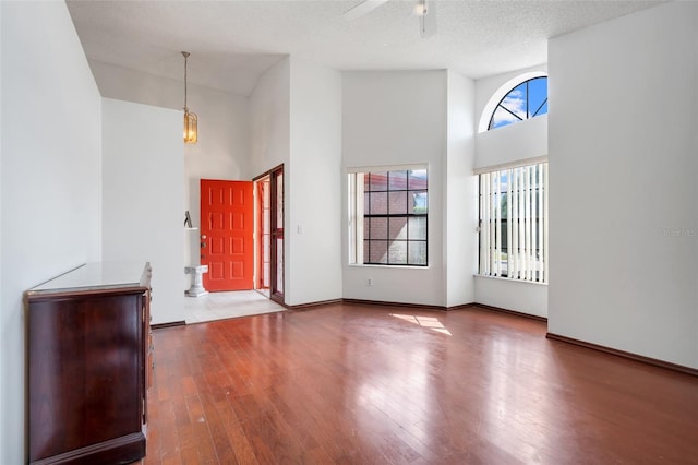 entrance foyer with ceiling fan with notable chandelier, a textured ceiling, a towering ceiling, and wood-type flooring