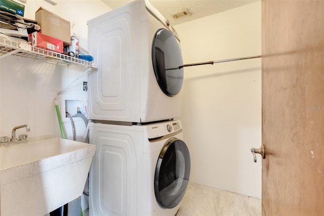 clothes washing area featuring visible vents, a sink, a textured ceiling, stacked washer / drying machine, and laundry area