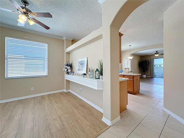 interior space with light wood-style flooring, ornamental molding, arched walkways, and a textured ceiling