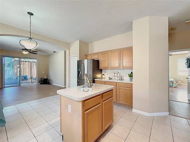 kitchen with arched walkways, ceiling fan, light countertops, stainless steel fridge, and open floor plan