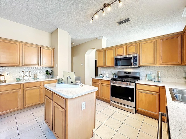 kitchen featuring light tile patterned floors, visible vents, arched walkways, stainless steel appliances, and a center island