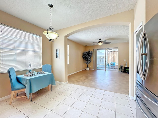 dining room featuring a ceiling fan, a textured ceiling, arched walkways, light tile patterned flooring, and baseboards