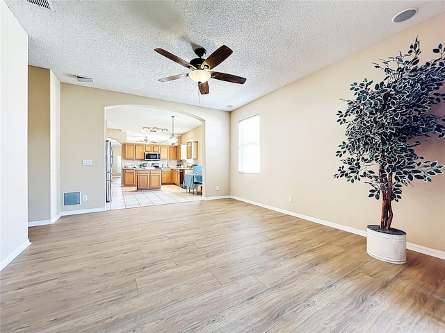 living area with arched walkways, light wood finished floors, a textured ceiling, and ceiling fan