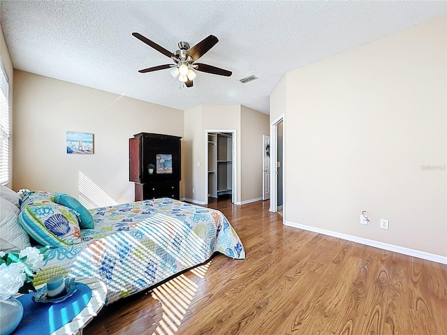 bedroom with a ceiling fan, baseboards, wood finished floors, visible vents, and a textured ceiling