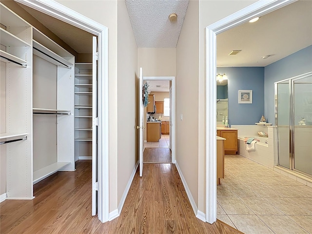 corridor featuring baseboards, visible vents, light wood finished floors, and a textured ceiling