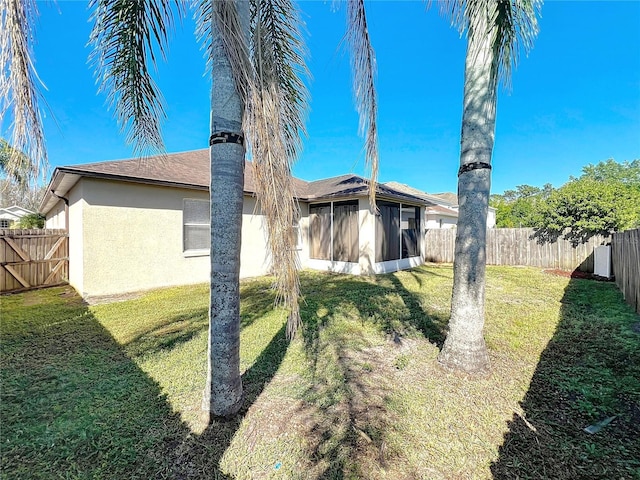 rear view of house with a shingled roof, a sunroom, stucco siding, a yard, and a fenced backyard