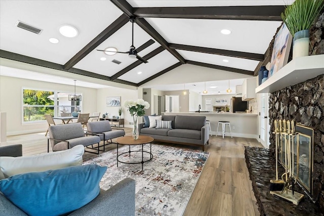 living area featuring visible vents, light wood-style flooring, a fireplace, and lofted ceiling with beams